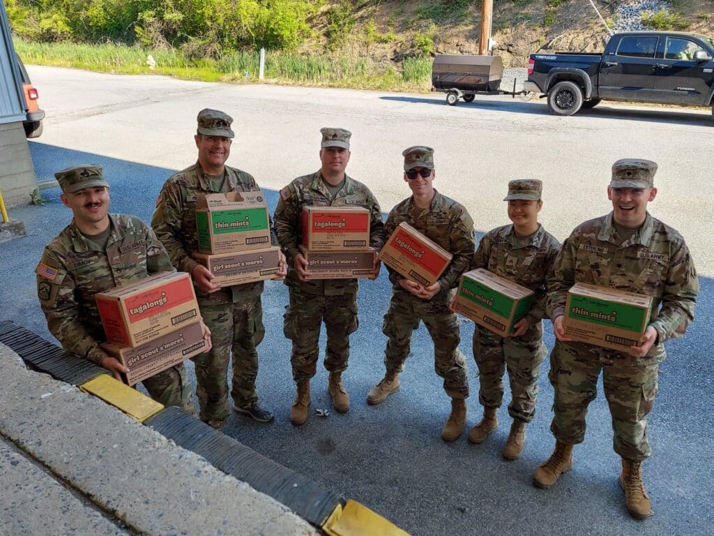 service members holding cases of Girl Scout cookies