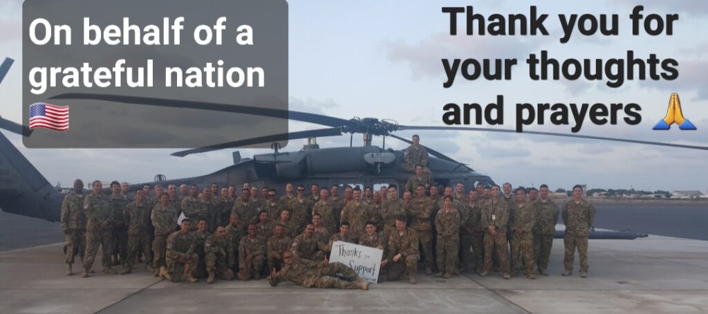 Deployed Unit of Service Members in front of a helicopter with a sign that says Thank You